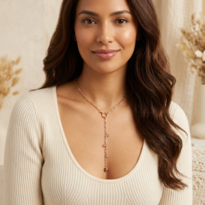 Gold lariat necklace with circular ring center and dangling crystal charm drop worn by a woman in a cream ribbed top