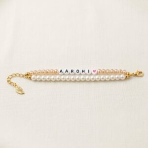 Double strand personalized name bracelet with white pearl beads, champagne crystal beads, letter beads spelling a custom name, heart charm, and gold leaf extender chain
