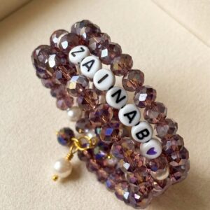 Multi-strand purple crystal bead bracelet stack with letter beads spelling a custom name and a pearl charm dangle