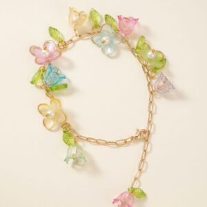 Flat lay of gold paperclip chain bracelet with multicolored pastel flower charms, pearl centers, bell flowers, and green leaf accents on cream background