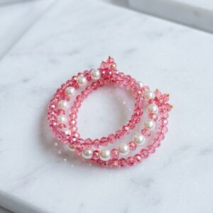 Set of two stretchy pink crystal and white pearl beaded bracelets with gold accent beads on marble surface