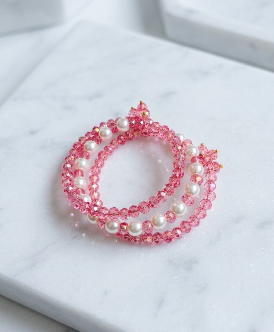 Set of two stretchy pink crystal and white pearl beaded bracelets with gold accent beads on marble surface
