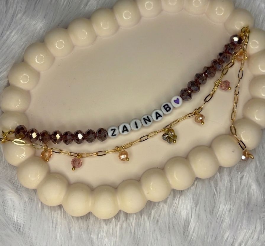 Personalised name bracelet with brown crystal beads, white letter beads spelling a name, and a gold paperclip chain with dangling crystal charms
