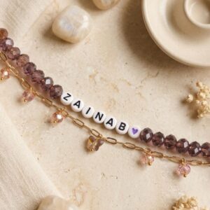 Personalised name bracelet with brown crystal beads, white letter beads spelling a name, and a gold paperclip chain with dangling crystal charms