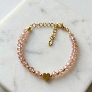 Pink faceted crystal bead bracelet with a gold heart charm and gold extender chain, displayed on a marble surface