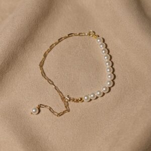 Half pearl half gold paperclip chain bracelet with lobster clasp and pearl drop extender, displayed on a beige fabric background