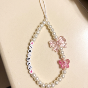 Personalised pearl bead phone charm with white letter beads spelling a name, pink iridescent bow charm and pink butterfly charm on a white cord loop