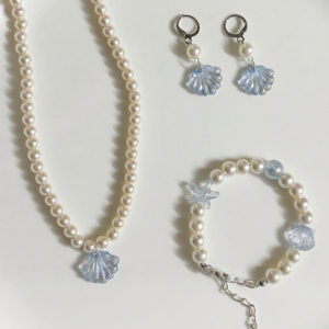 Pearl Tide Shell jewellery set featuring a glass pearl necklace with a blue shell charm, adjustable glass pearl bracelet with blue shell and starfish-inspired charms, and matching pearl and blue shell earrings, displayed on a white background.